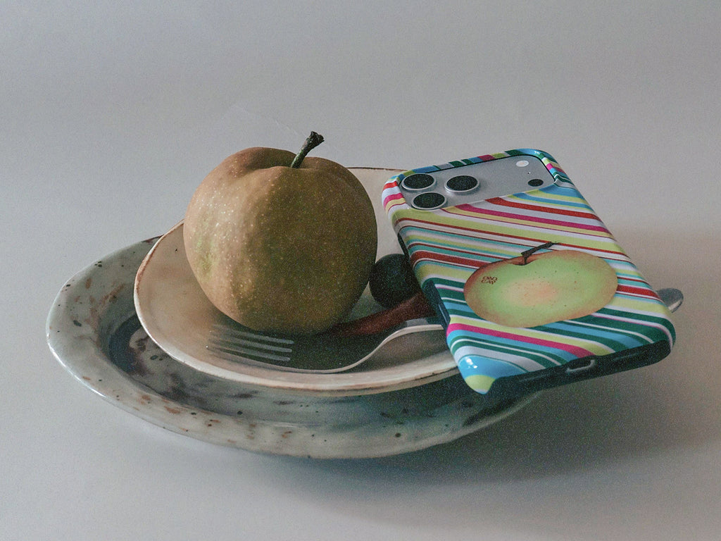 Apple for Later striped MagSafe phone case beside a real apple and tableware